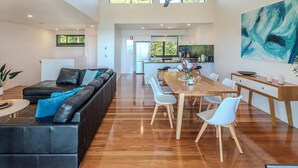 A spacious living area with a black leather sofa, a wooden dining table, and white chairs. - Pinnacle 3, Seaview Apartment on Hamilton Island (Hamilton Island)