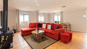 A living room with a red sofa, a round coffee table, and a black fireplace. - The Cottage @ Hunter Gleann - Much more than the average cottage! (Pokolbin)
