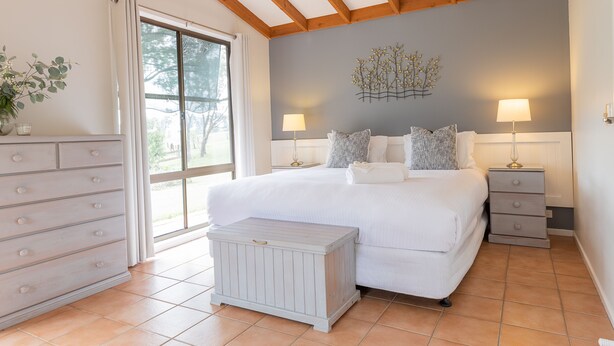 A bedroom with a large bed, two bedside tables with lamps, a dresser, and a window with curtains. - The Cottage @ Hunter Gleann - Much more than the average cottage! (Pokolbin)