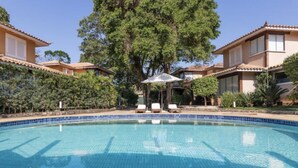 Une piscine dont les bords sont recouverts de carreaux, entourée de chaises longues et d’un grand arbre.