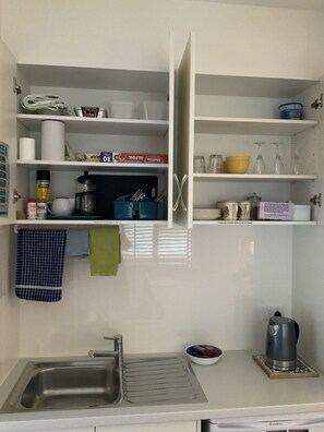 Eine Küche mit Spüle, Wasserkocher und verschiedenen Küchenutensilien in Regalen.