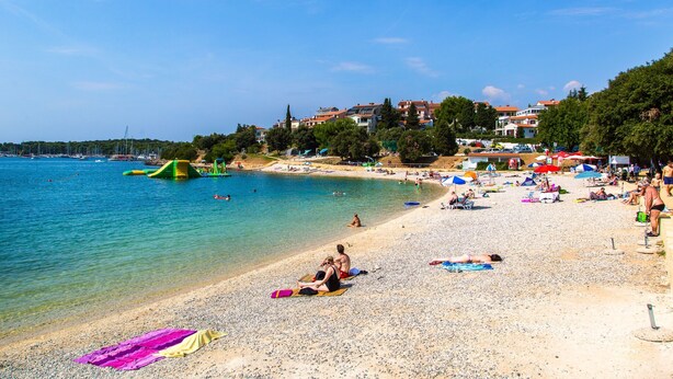 Une plage avec une eau d’un bleu limpide, des gens qui prennent des bains de soleil et des parasols de plage.