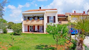 Une maison à deux étages, avec un toit en tuiles, un balcon et un petit jardin.