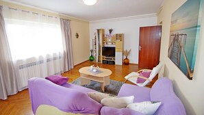 Un salon avec un canapé violet, une table basse en bois et un meuble pour la télévision, sur lequel est posé un téléviseur à écran plat.