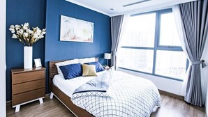 Un dormitorio moderno con una cama grande, una mesita de noche, un jarrón de flores y vistas a la ciudad desde la ventana.