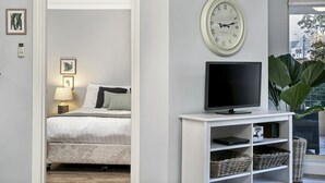 A bedroom with a bed, a TV on a white stand, a clock, and a plant.