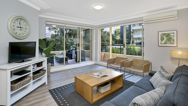 A modern living room with a flat-screen TV, a sofa, a coffee table, and a balcony with outdoor furniture.