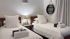 Hotellihuone, jossa on kaksi sänkyä, valkoiset vuodevaatteet, yöpöytä lampun kanssa, peili ja pyyhe jokaisella sängyllä.
