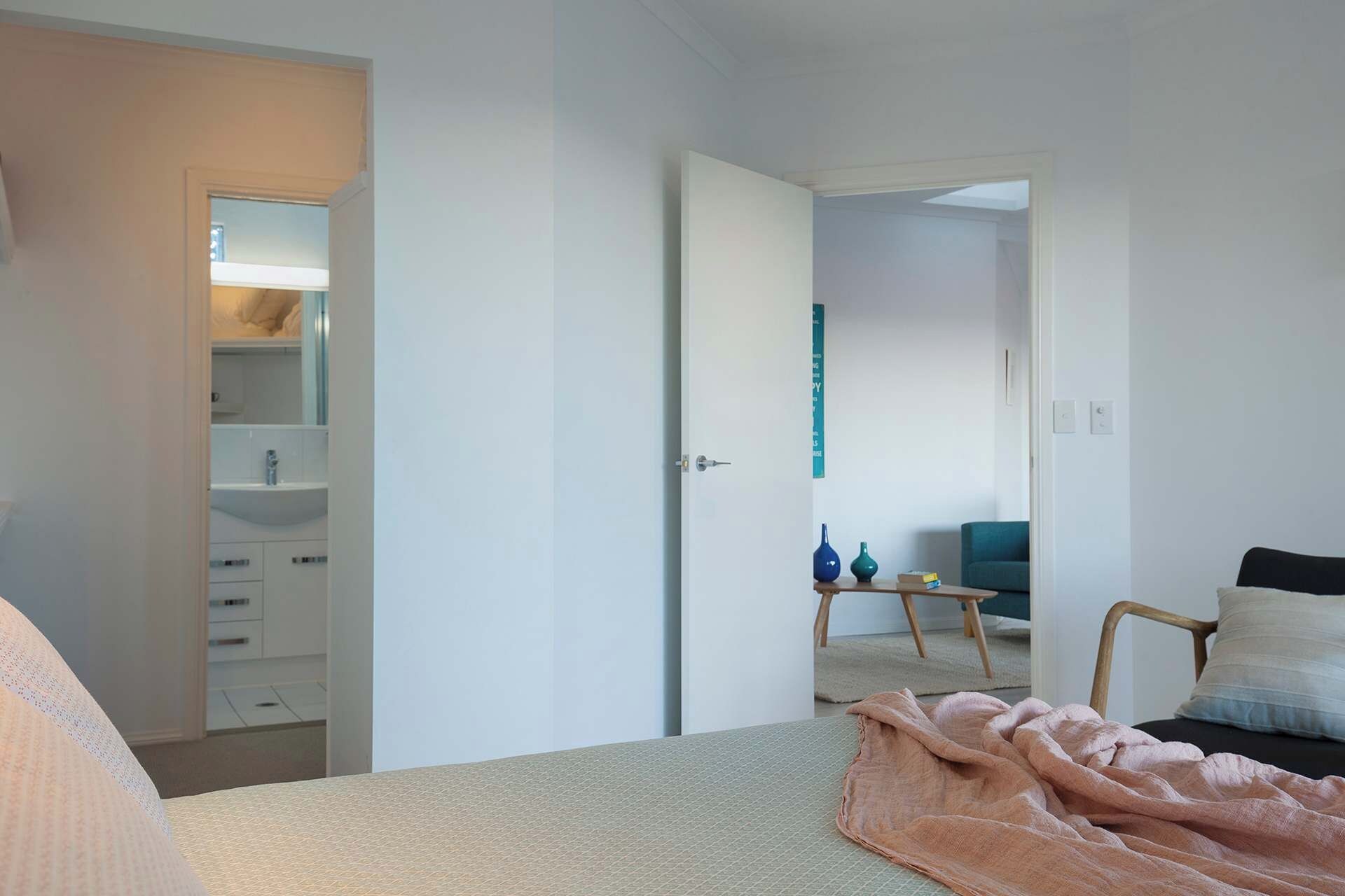 A bedroom with a bed, a bedside table, a chair, a wardrobe, and a bathroom visible through an open door.