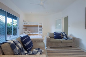 A room with a bunk bed, a wicker sofa, and a window with a view of greenery.