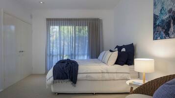 A bedroom with a bed, a bedside lamp, a chair, and a large window with curtains.