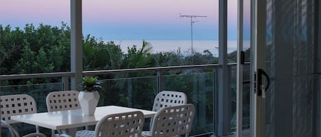 A balcony with a table and chairs, overlooking a body of water and greenery.