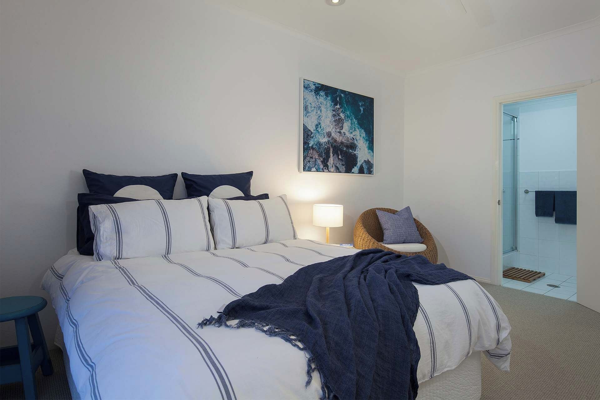 A bedroom with a bed, pillows, a chair, a lamp, and a door leading to a bathroom.