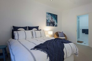 A bedroom with a bed, pillows, a chair, a lamp, and a door leading to a bathroom.