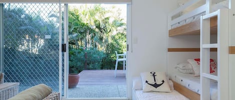 A room with a sliding glass door leading to a patio, a bed with a white headboard, a wicker sofa, and a small table.