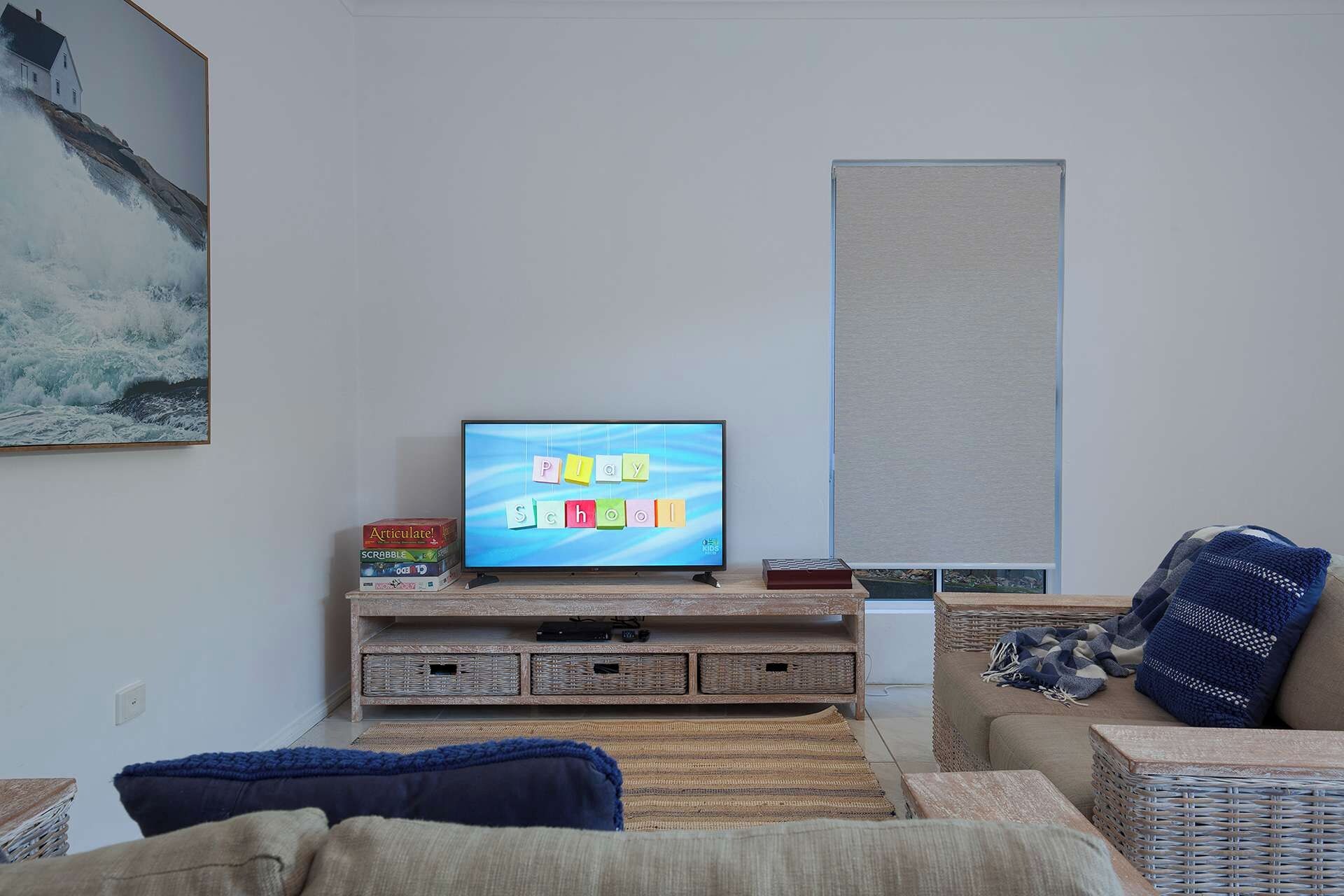 A living room with a television displaying a children's game, a bookshelf, a sofa, and a painting on the wall.