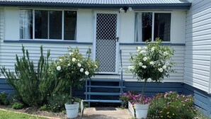 Ein Haus mit Veranda, einer Metalldür und zwei Blumentöpfen mit weißen Blüten.
