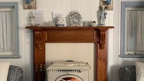 Ein gemütliches Zimmer mit einem weißen Kamin, einem Gemälde darüber und einem Kaminbrett, das mit kleinen Figuren und einer Uhr dekoriert ist.
