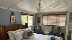 Ein gemütliches Schlafzimmer mit einem hölzernen Bett, zwei Stühlen, einem kleinen Tisch und einer Deckenleuchte.