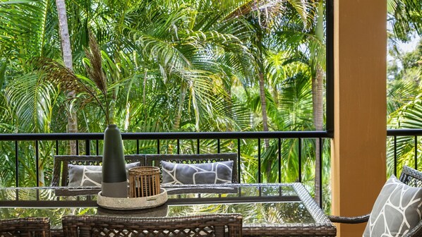 Un balcón con mobiliario de mimbre, un jarrón y vistas de una vegetación tropical exuberante.