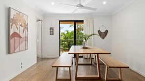 A modern dining area with a wooden table and benches, a ceiling fan, and a view of lush greenery outside.