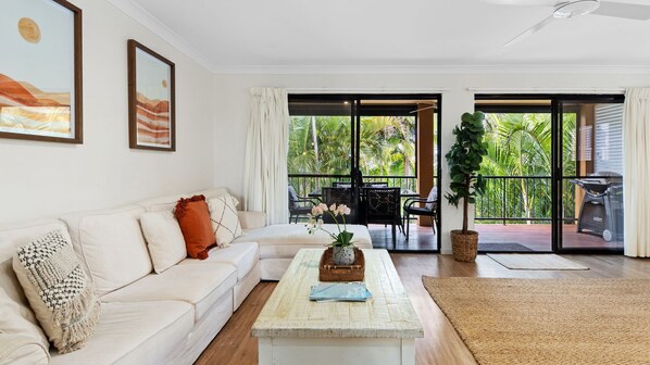 A modern living room with a white sofa, a coffee table with a plant, and a balcony with a grill.