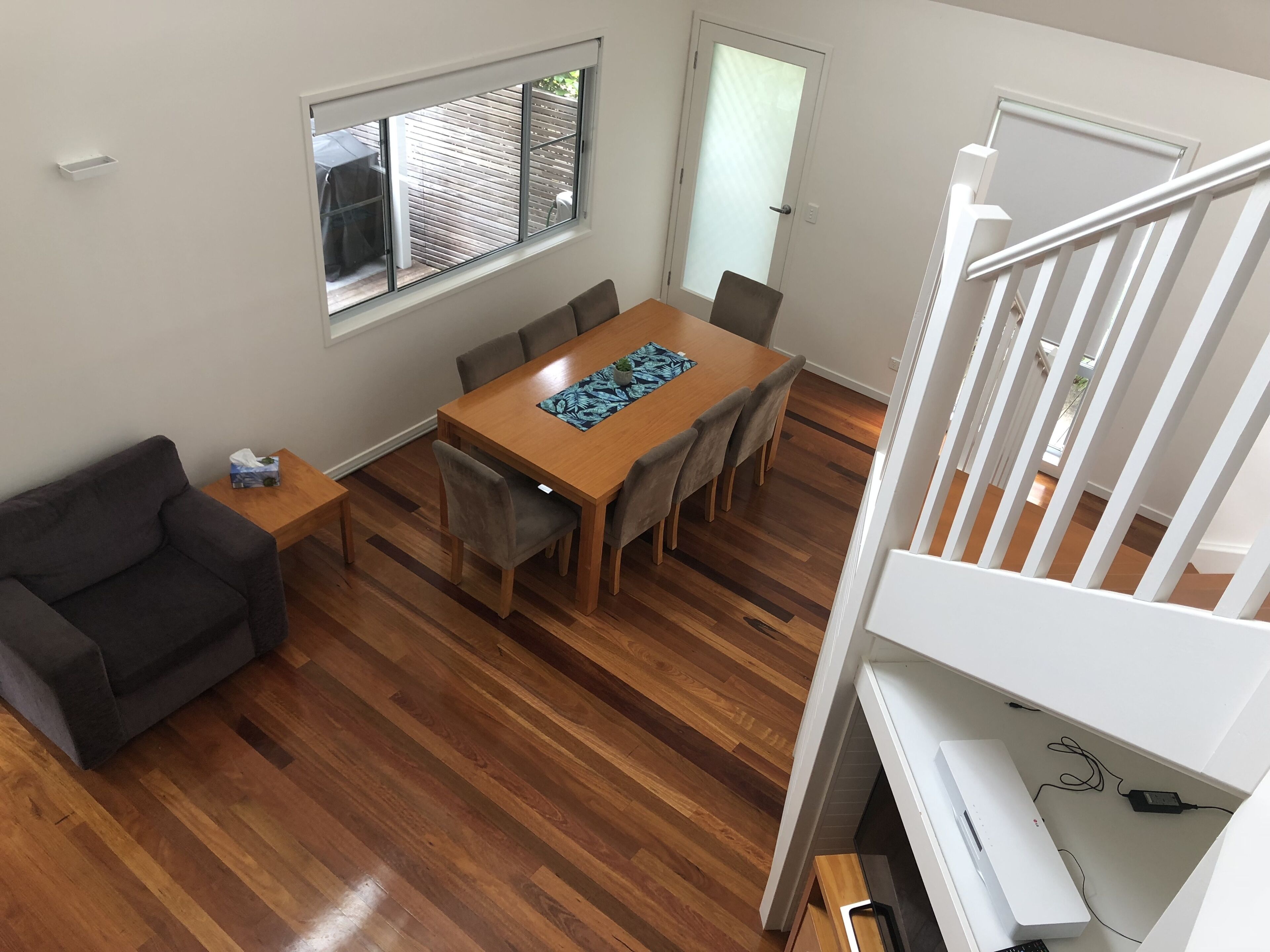 A dining area with a wooden table and chairs, a sofa, and a window with blinds.