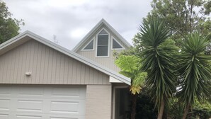 Una casa con un garage, un tetto a punta e un giardino con palme.