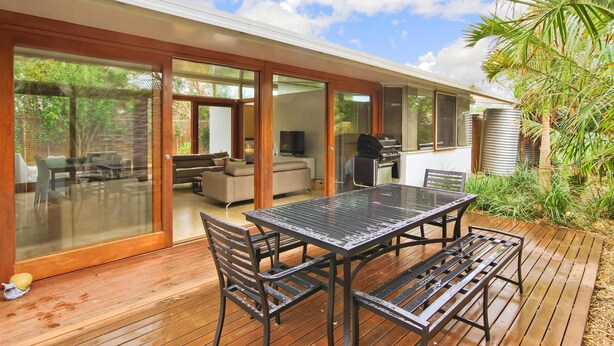 A modern outdoor patio with a glass-enclosed dining area, a barbecue grill, and a wooden deck.
