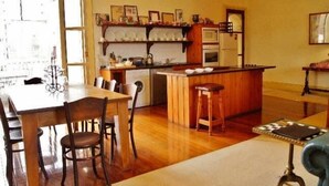A kitchen with a wooden island, chairs, a dining table, and a refrigerator. - Fire Station Inn Penthouse Spa Apartment (North Adelaide)