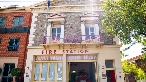 A fire station with a classic architectural style, featuring a stone facade, a red fire truck parked in front, and a flagpole with a flag. - Fire Station Inn Penthouse Spa Apartment (North Adelaide)