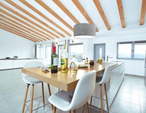 Une cuisine moderne avec un plafond en bois, des chaises blanches, un îlot central et un luminaire suspendu.