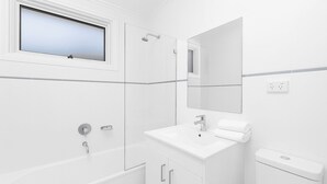 A modern bathroom with a bathtub, a sink, and a toilet. There is a window above the bathtub and a mirror above the sink. - Mosman BOT01 Botanic Rd-Balmoral 2BR Balcony Steps from Balmoral Beach Esplanade (Mosman)