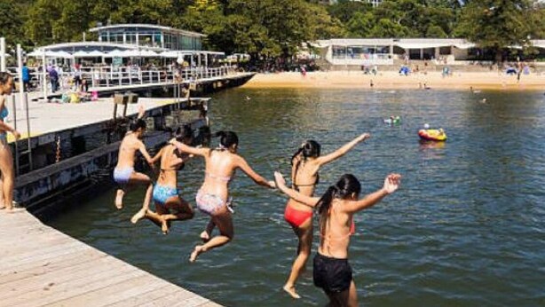A pier with people jumping into the water, a boat docked, and a beach in the background. - Mosman BOT01 Botanic Rd-Balmoral 2BR Balcony Steps from Balmoral Beach Esplanade (Mosman)