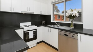 A modern kitchen with white cabinets, a black countertop, a stove, a sink, and a window with a view of buildings. - Mosman BOT01 Botanic Rd-Balmoral 2BR Balcony Steps from Balmoral Beach Esplanade (Mosman)