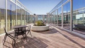 A modern outdoor patio with glass walls, a wooden deck, and a central planter with plants. - Fawkner Residence 1B1B Condo with Pool&Gym Access (Melbourne)
