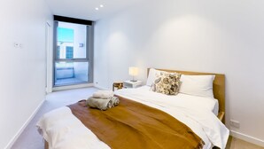 A modern hotel room with a large bed, a window with a view, a bedside table with a lamp, and a brown throw blanket. - Fawkner Residence 1B1B Condo with Pool&Gym Access (Melbourne)