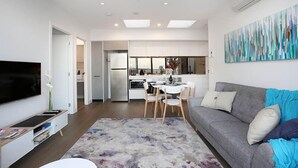 A modern living room with a flat-screen TV, a grey sofa, and a dining area with a white table and chairs.