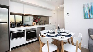 A modern kitchen with white cabinetry, a dining table set for four, and a large window above the sink.