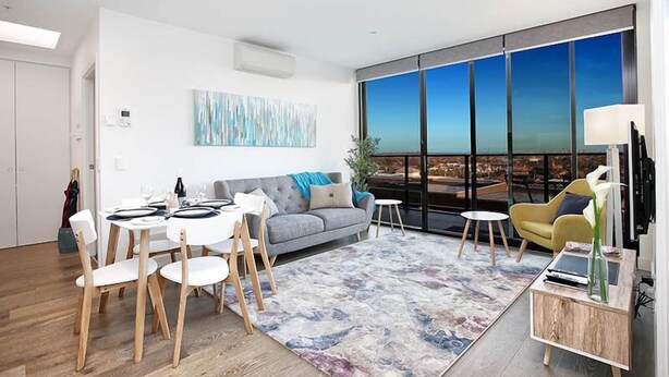 A modern living room with a dining area, large windows, and a city view.