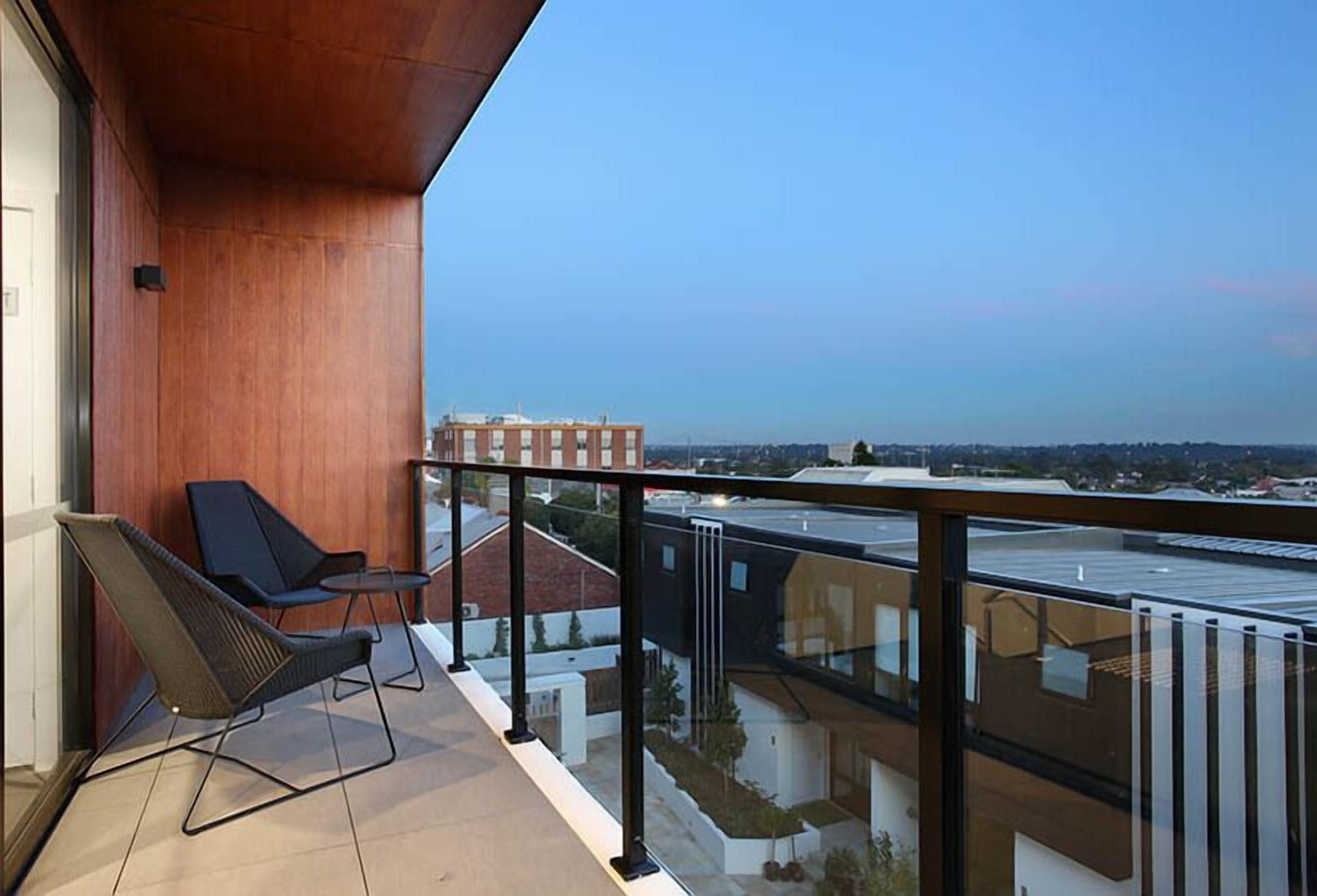 Un balcon avec deux chaises et une balustrade en verre donnant sur un paysage urbain.