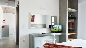 A modern hotel room with a bed, a desk, a chair, a television, and a wardrobe. - Kota Villa with private pool (Santorini)