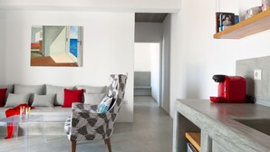 A modern living room with a sofa, a patterned armchair, a coffee machine, and a painting on the wall. - Kota Villa with private pool (Santorini)