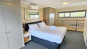 Ein Schlafzimmer mit Bett, Kleiderschrank, Spiegel, Fenster und fest eingebautem Schreibtisch.