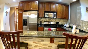 A kitchen with wooden cabinets, a stainless steel refrigerator, a microwave, and a stove. There are two wooden chairs with cushions. - Second-Floor Pool-View Condo – Your Perfect Beach Retreat in Jacó (Jacó)