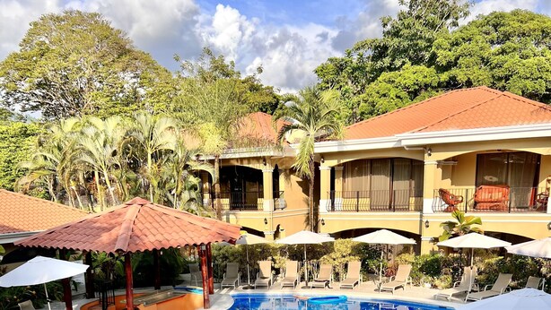 A resort with a large, multi-tiered swimming pool surrounded by lounge chairs and umbrellas, with a building featuring balconies in the background. - Second-Floor Pool-View Condo – Your Perfect Beach Retreat in Jacó (Jacó)