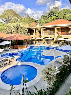 Ein Resort mit einem großen, mehrstufigen Pool, umgeben von Liegestühlen und Sonnenschirmen, mit einem Gebäude mit Balkonen im Hintergrund.