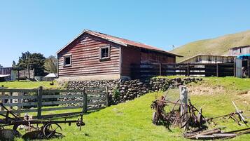 A rustic wooden barn with a sloped roof, surrounded by a stone wall and a wooden fence.
