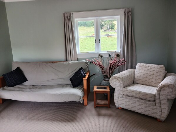 A living room with a sofa, a patterned armchair, a small wooden side table, and a vase with decorative branches. - Devcich Historic Farmstead - Cottage (Thames)