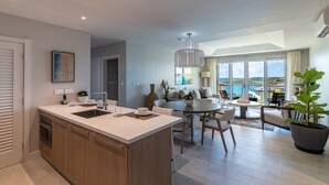 Una cocina moderna con una isla central, zona de comedor con una mesa redonda y un ventanal con vistas al mar.
